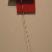 Papier rouge en forme de maison, avec une petite porte et un petit escalier, suspendu à un fil de fer